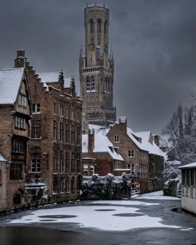 The same corner of Bruges in winter: snow on the roofs, the canal frozen over and the belfry cut out against a leaden sky.