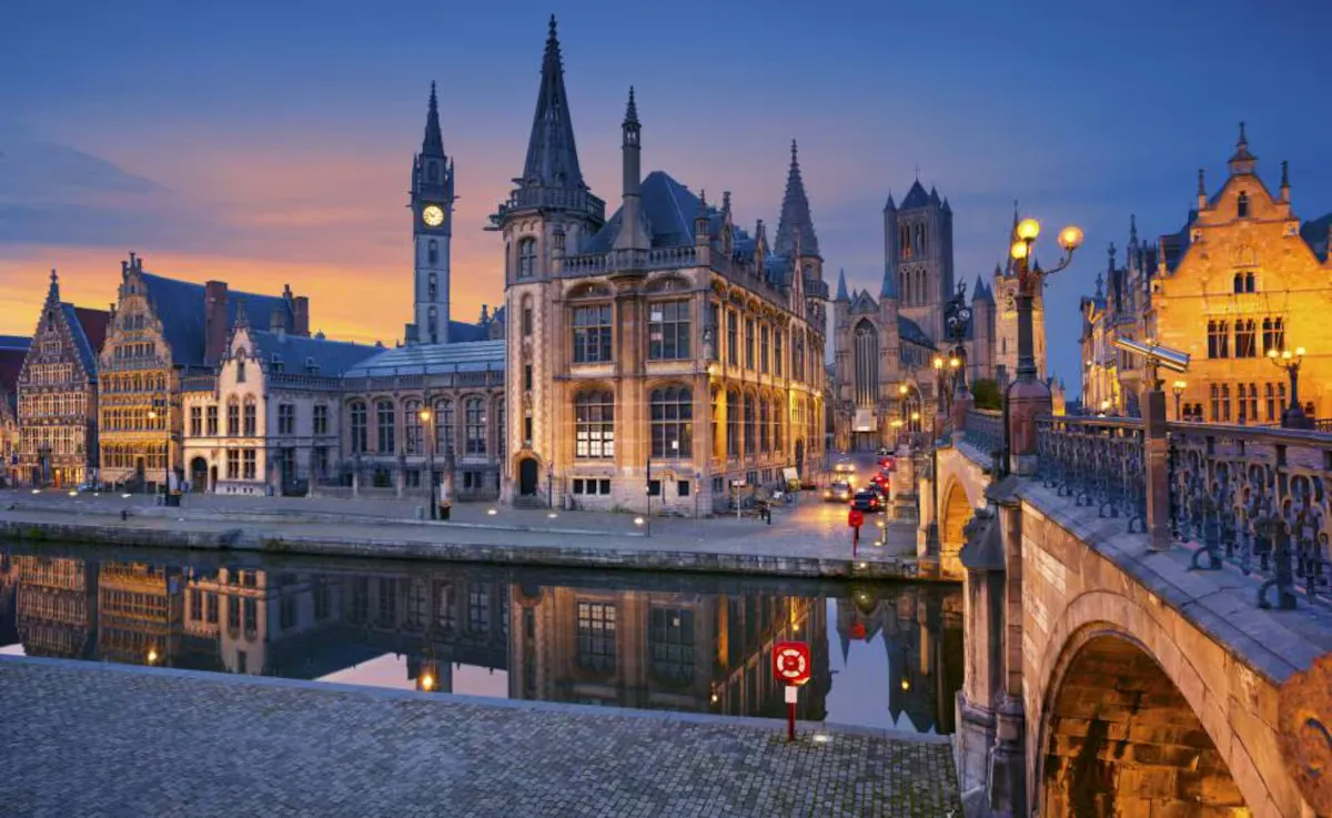 The Graslei in Ghent at dusk, guild façades reflected in the water.