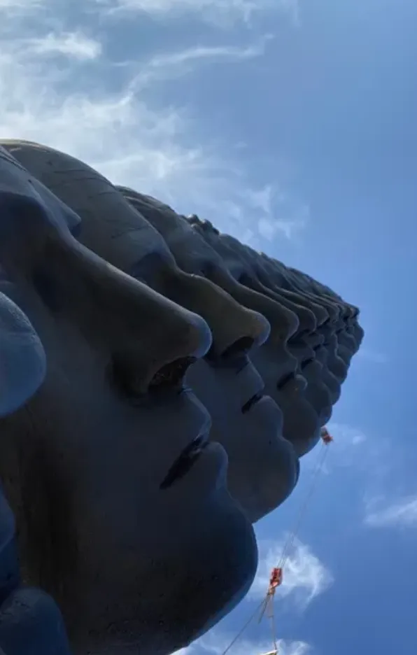 Bronze sculpture of several stacked heads looking upward.